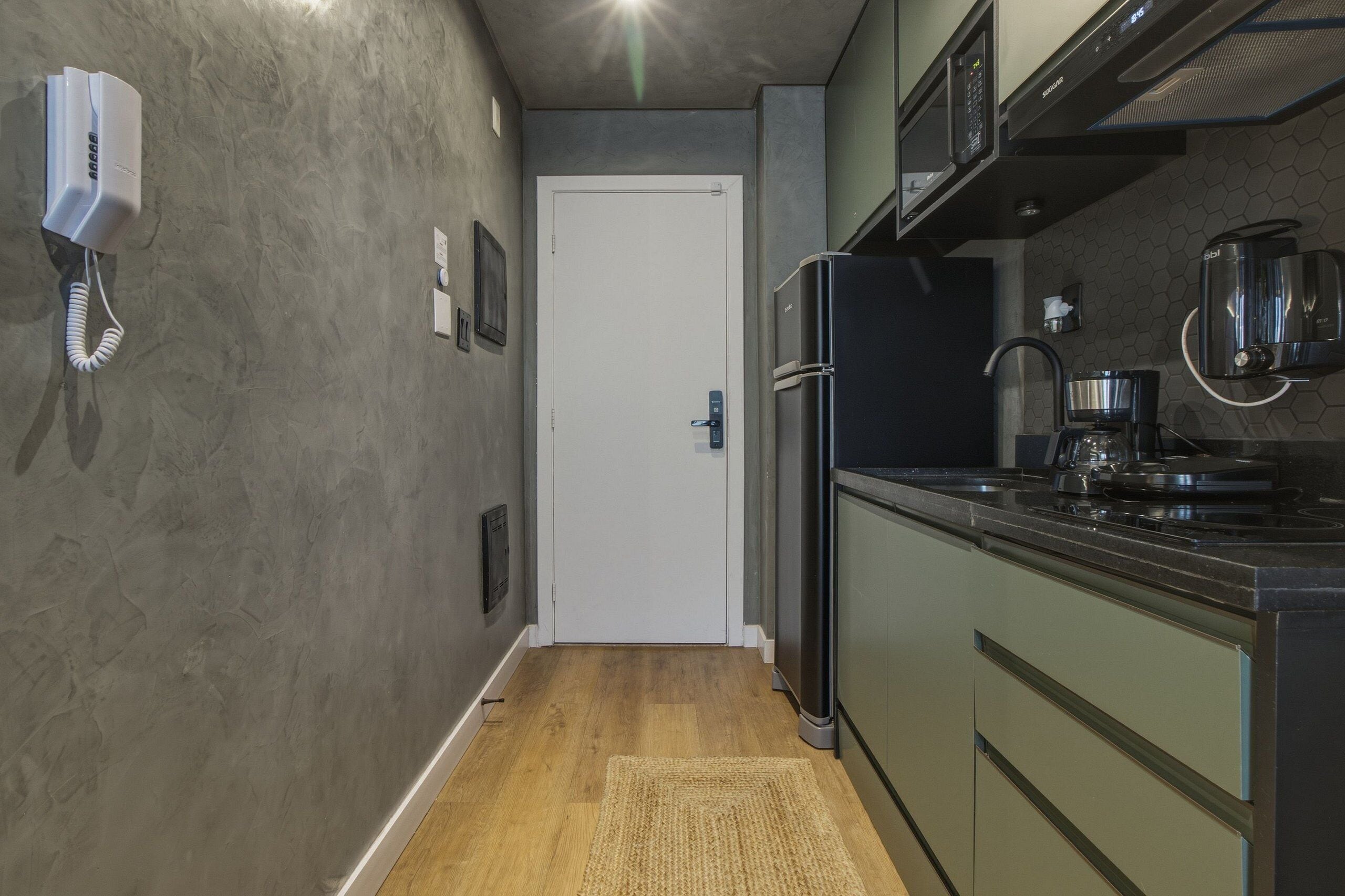 A kitchen with a refrigerator, microwave, coffee maker, and a phone on the wall.