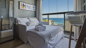 Een moderne slaapkamer met een groot raam, een bed met opgerolde handdoeken, een nachtkastje en een lijst met kunstwerk aan de muur.