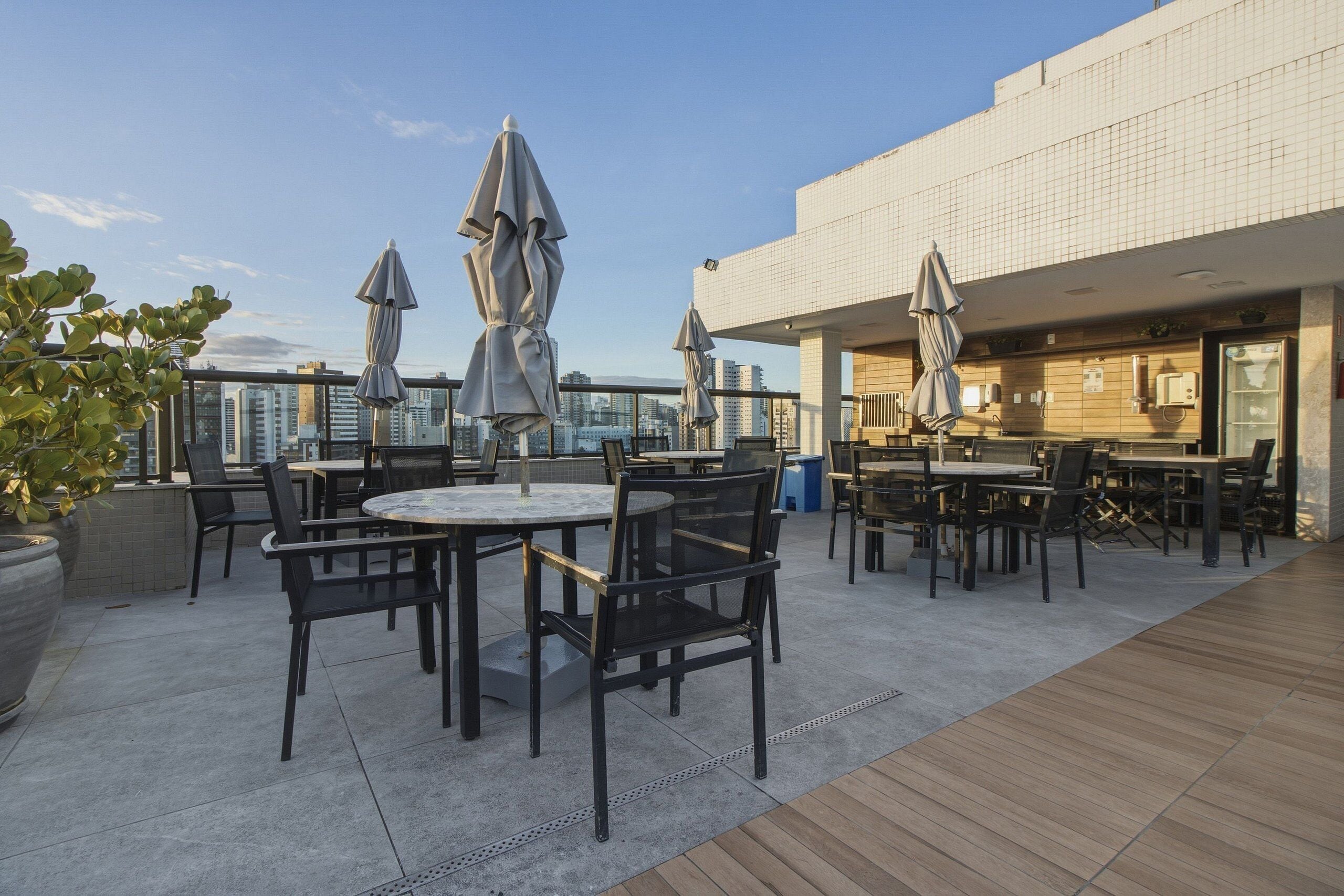 Eine Dachterrasse mit Sitzgelegenheiten im Freien, Sonnenschirmen und Blick auf die Stadtlandschaft.