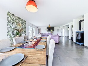 Ein modernes Wohnzimmer mit Essbereich, einem großen Flachbildfernseher, einem Kamin und einer Treppe, die zu einer weiteren Ebene führt.