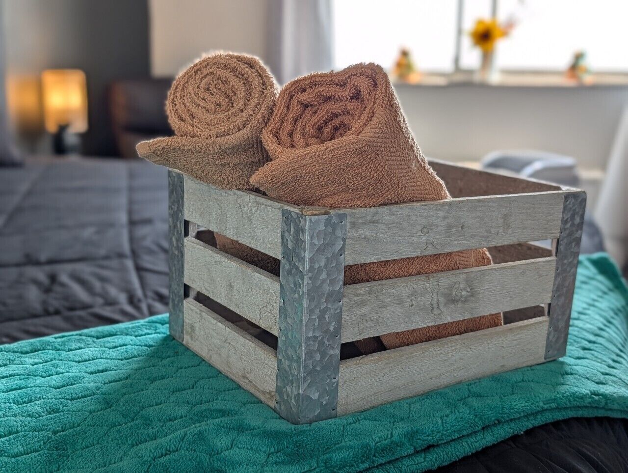 A rustic wooden crate with two rolled towels on top, placed on a teal blanket.