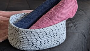 Un panier en tricot contenant trois serviettes pliées, posé sur un lit.