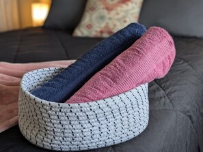 Een gebreide mand met drie opgevouwen handdoeken op een bed.