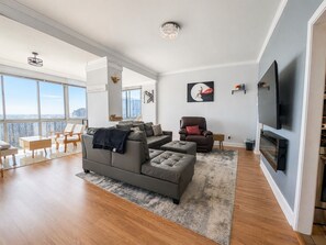 A modern living room with a grey sofa, a brown armchair, and a flat-screen TV mounted on the wall.