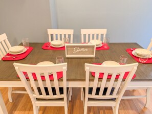 Une table à manger dressée pour six personnes, avec des chaises blanches et des sets de table rouges.