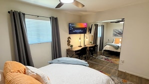 A bedroom with a bed, a desk, a chair, a ceiling fan, a TV, and a mirror. - Tempe Oasis w Pool, Spa and Garage! (Tempe)