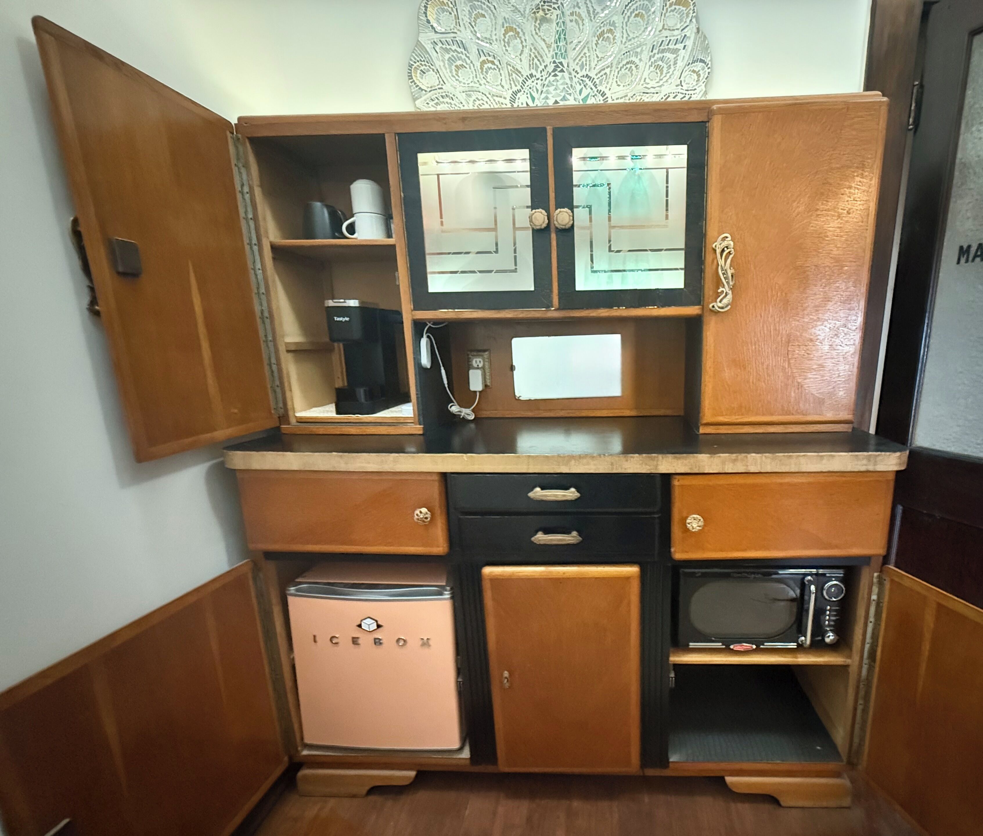 A compact kitchenette with a refrigerator, microwave, coffee maker, and a small icebox.