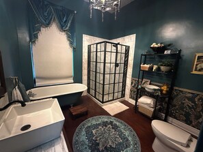 Un baño con una bañera independiente, cabina de ducha, inodoro y un estante con artículos de aseo.