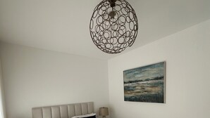 Una cama bien hecha con sábanas blancas, dos almohadas y toallas enrolladas. Hay un cuadro colgado en la pared y una lámpara circular original sobre la cama.