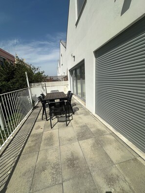 A patio with a table and chairs, a garage door, and a white building. - Home Sweet Home. (Parchal)