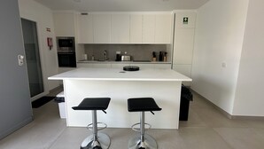 Una cocina moderna con armarios blancos, una isla central con taburetes, horno empotrado y extintor.