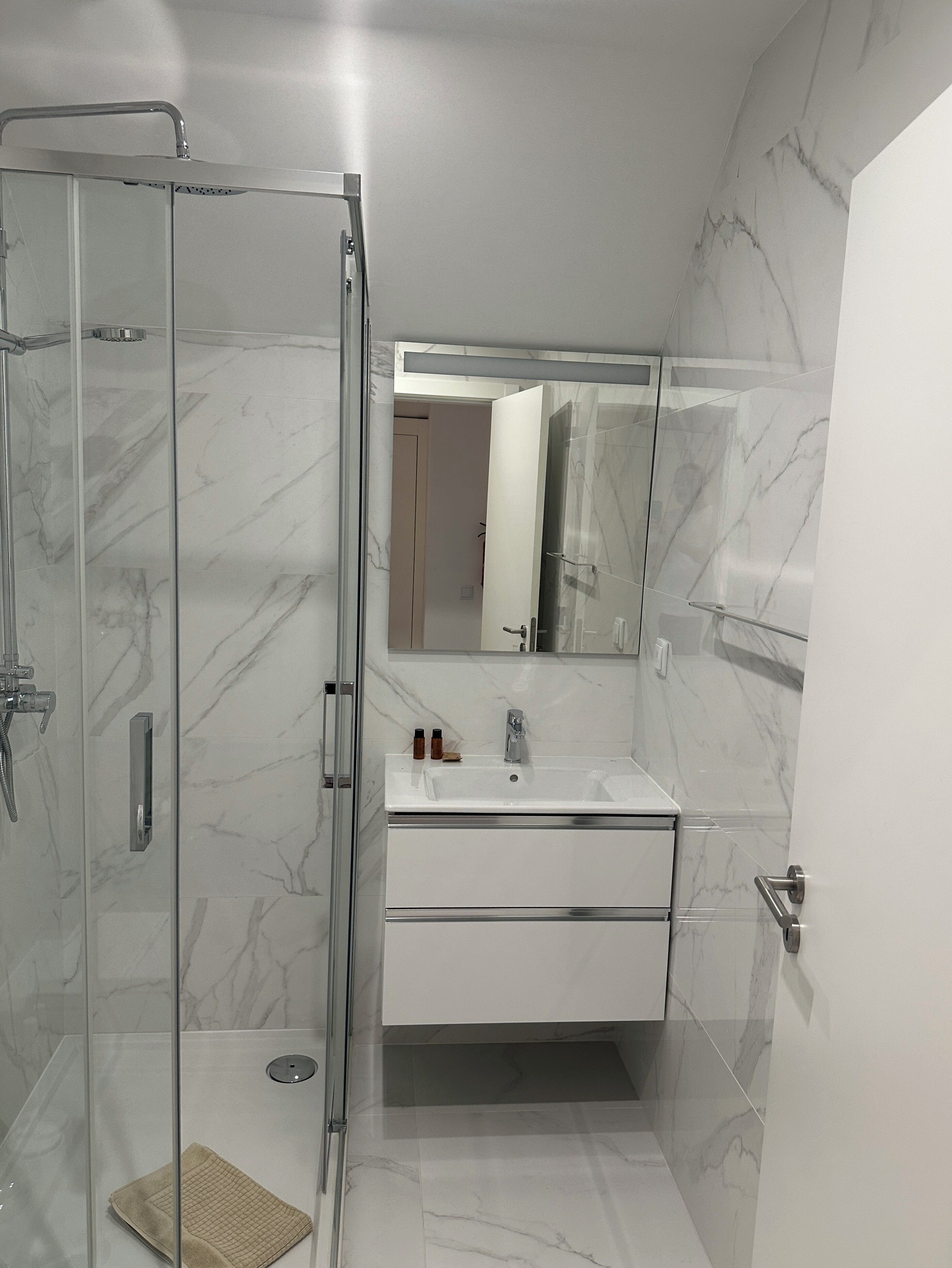 Ein modernes Badezimmer mit einer Duschkabine aus Glas, einem weißen Waschbecken und einem Boden mit Marmorfliesen.