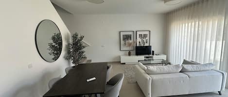 A modern living room with a dining area, a sofa, a TV, and a potted plant.
