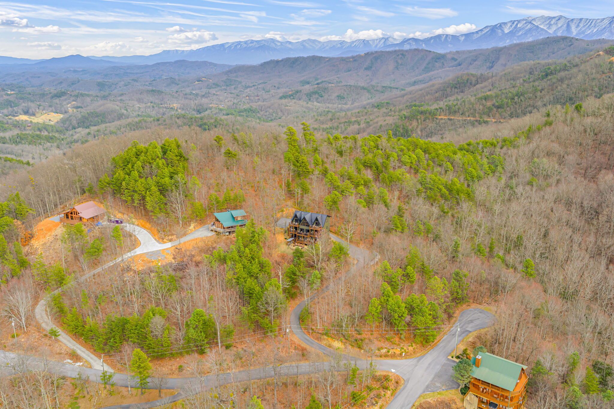 A cabin complex with multiple buildings, surrounded by a forested area with winding roads.