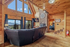 Ein Holzinnenraum mit einer Couch, einem Kamin aus Stein und einem großen Fenster mit Blick auf eine schöne Landschaft.