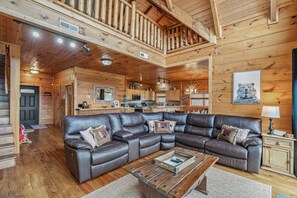 Ein Holzblockhaus-Interieur mit einem ledernen Ecksofa, Holzböden, einer Küchenzeile und einer Erschliessungsebene mit Holzwertlauf.