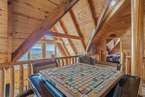 Ein Holzinterieur mit einem großen Gesellschaftsspiel-Tisch, Holzbalken und einem Fenster mit Blick auf eine Landschaft.