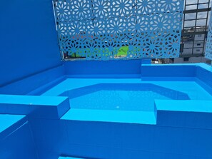 En blå utomhuspool med ett geometriskt mönster, omgiven av en blå vägg och ett dekorativt metallstaket.