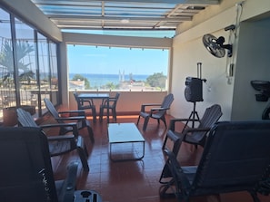 Un balcón con mesa y sillas, un ventilador y vista al mar.
