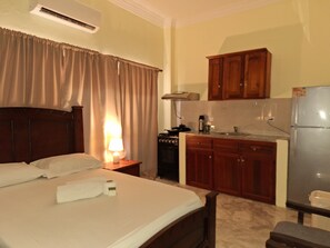Ein Hotelzimmer mit einem Bett, einem Nachttisch mit Lampe, einer Küchenzeile mit Herd und Holzschränken.