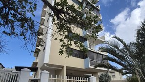 En bygning med flere etager, en lukket indgang, en blå væg med et logo og et træ i forgrunden.