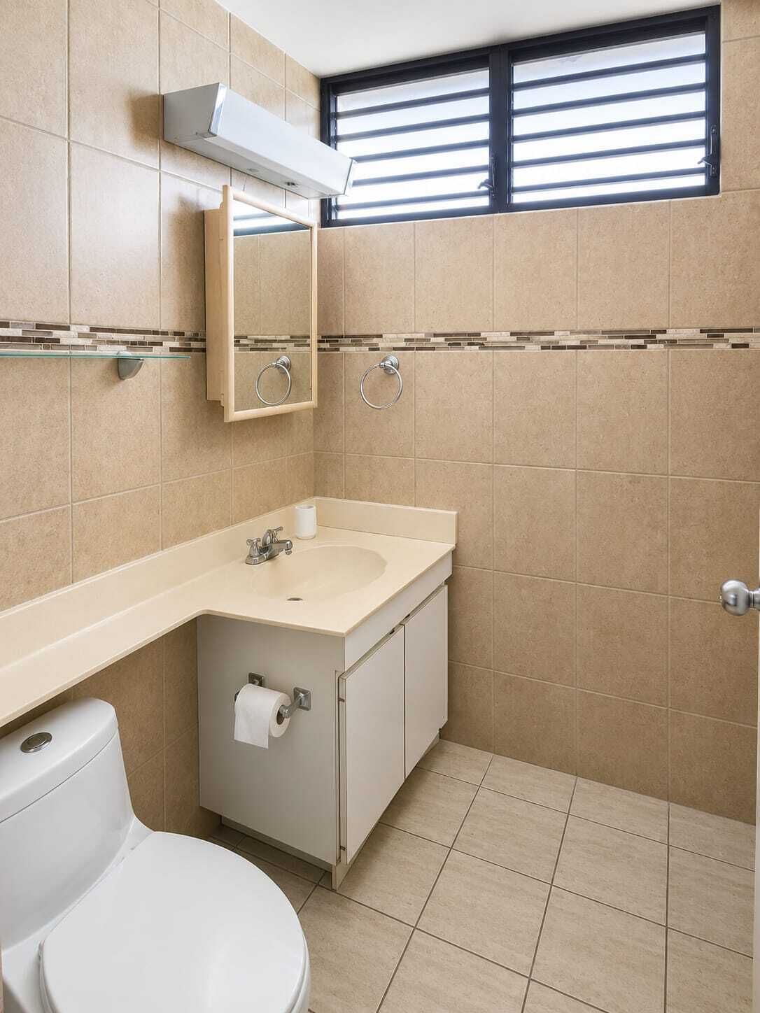 A bathroom with a toilet, sink, mirror, towel rings, and a window with blinds.