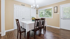 A dining room with a table, chairs, a chandelier, and a window with blinds.