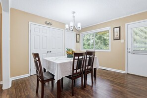 Une salle à manger avec une table, des chaises, un lustre et une fenêtre avec des stores.