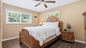 A bedroom with a wooden bed, a nightstand, a dresser, a ceiling fan, and two windows with blinds.