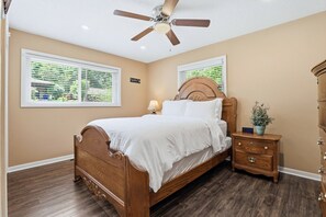A bedroom with a wooden bed, a nightstand, a dresser, a ceiling fan, and two windows with blinds. - Peaceful North Little Rock Home w Backyard! (North Little Rock)