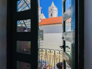 Blick durch eine Tür mit einem Metallgitter, ein Gebäude mit roten Ziegeln und ein weißer Turm mit einer Glocke.