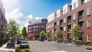 Moderni kaupunkikatu, jossa on useita kerroksia sisältäviä tiilitaloja, suojatie ja kadun reunassa pysäköity auto.