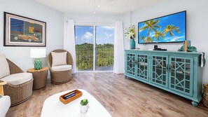 A living room with wicker furniture, a television, and a view through a glass door. - Sol & Sea Escape Ocean Pointe 1 BR 1BA 1204 (Tavernier)