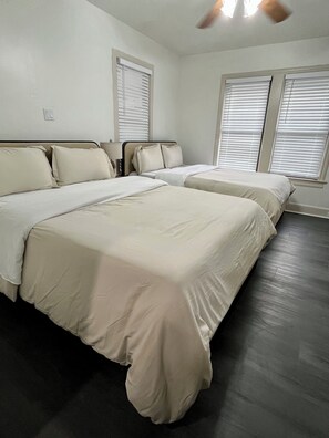 Ein Schlafzimmer mit zwei Betten, einem Deckenventilator und Fenstern mit Jalousien.