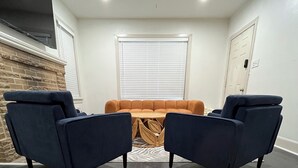 Una habitación con piso de madera oscura, ventilador de techo, ventana con persianas y un sofá marrón.