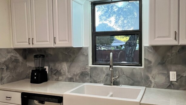 Una cocina con gabinetes blancos, lavavajillas integrado, ventana con vistas y encimera con licuadora.