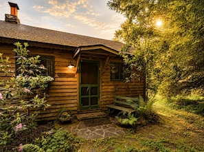 A wooden cabin with a green door, a stone pathway, and a bench outside.