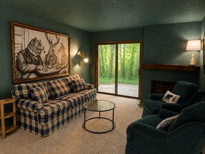 Un salon avec un canapé à carreaux, une table basse ronde, un fauteuil sombre, une cheminée et un grand tableau encadré représentant des animaux sauvages.