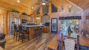 A spacious wooden cabin interior with a large dining table, bar stools, and a kitchen area. - Bears Haven Lodge (Sevierville)