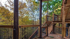 A wooden deck with a staircase leading to a higher level, surrounded by trees with autumn foliage. - Bears Haven Lodge (Sevierville)
