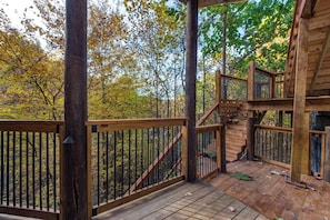 Eine Holzterrasse mit einer Treppe, die zu einer höheren Ebene führt, umgeben von Bäumen mit Herbstlaub.