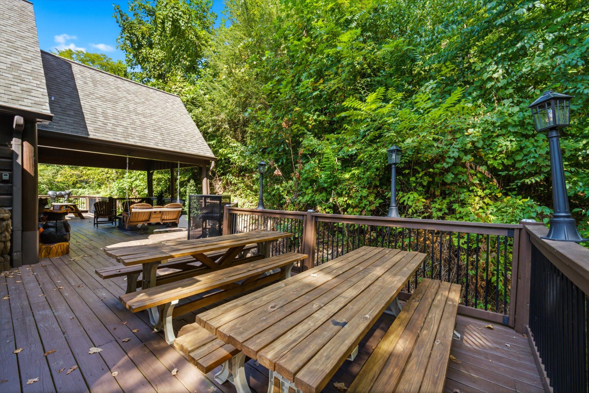 A wooden deck with picnic tables and a covered seating area, surrounded by lush greenery.