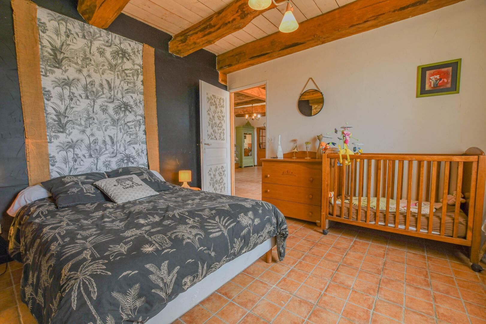A bedroom with a bed, a crib, a dresser, and a door leading to another room.