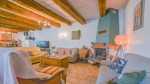 Een gezellige woonkamer met een open haard, houten balken, een televisie en een eethoek.