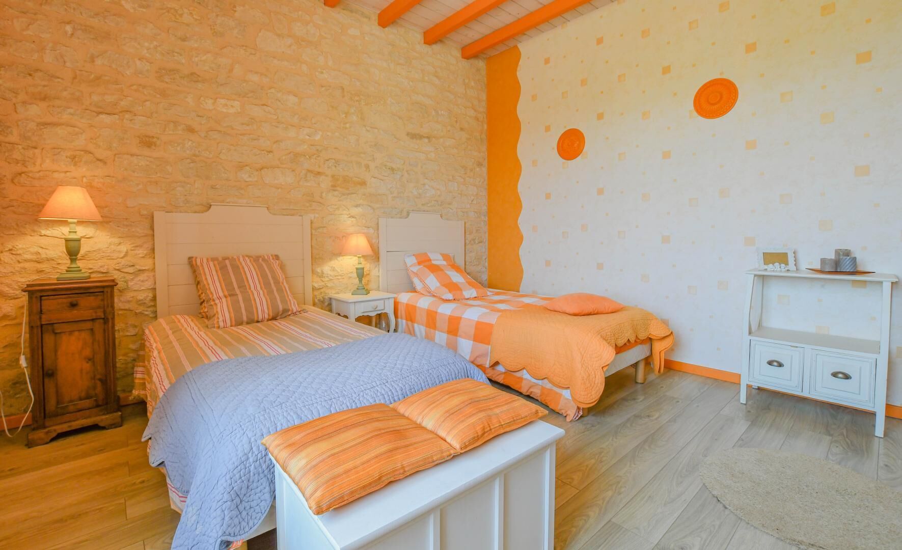 Une chambre avec deux lits, une table de chevet, une commode et un mur orné de motifs circulaires.