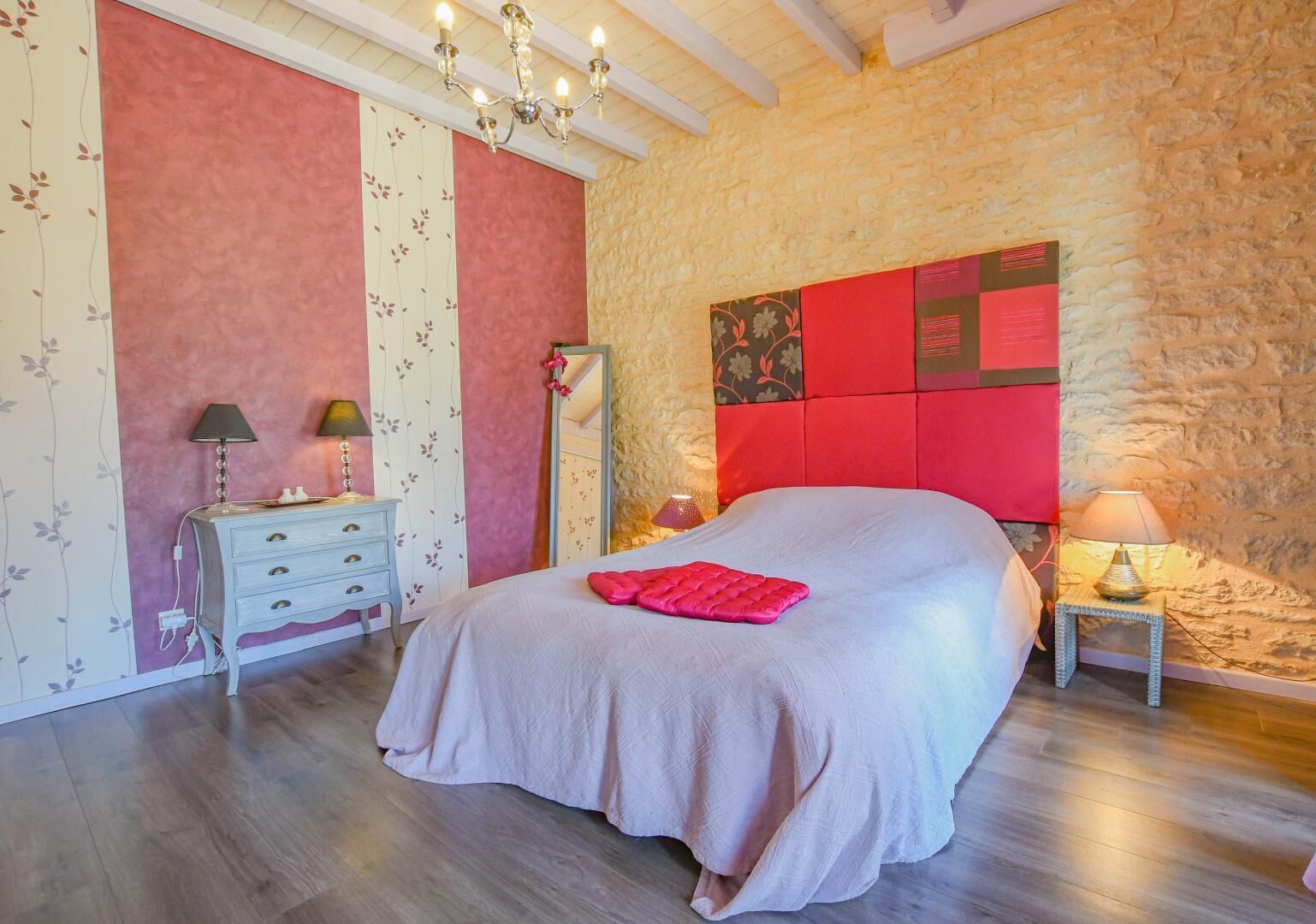 A bedroom with a large bed, a dresser, a mirror, and a chandelier.