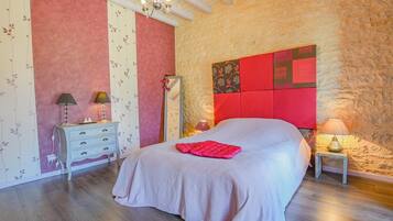 A bedroom with a large bed, a dresser, a mirror, and a chandelier.