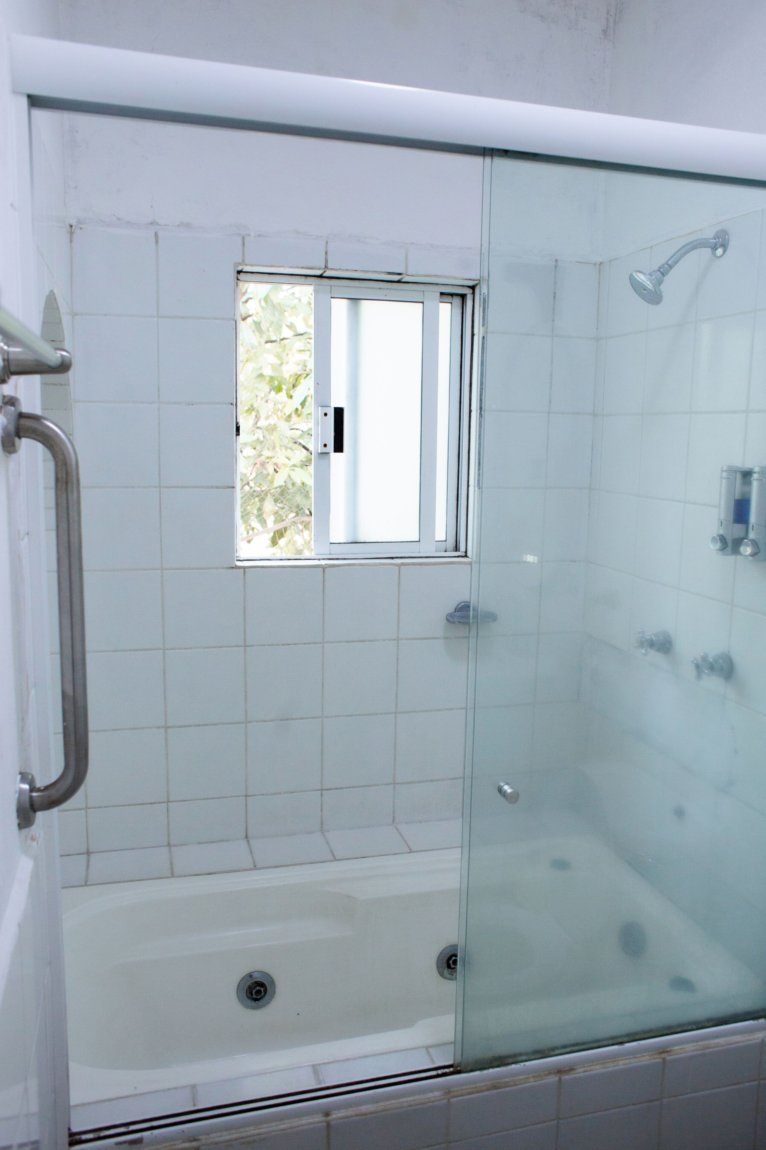 A glass-enclosed shower area with a window, a bathtub, and a handrail.