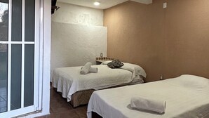 Habitación de hotel con dos camas, un ventanal corredero, un televisor pequeño y una lámpara en el techo.