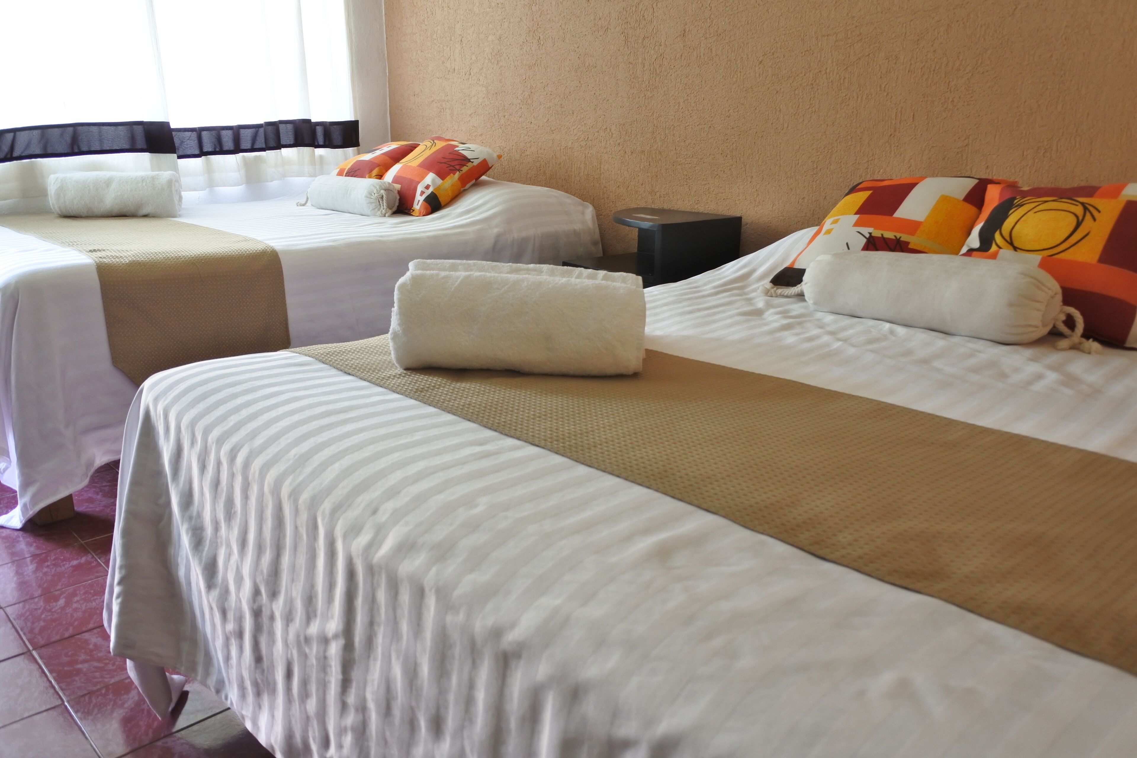 A hotel room with two beds, each with a white bedspread and pillows, and a small bedside table.